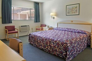 A hotel room with a bed, two chairs, a desk, a lamp, and a window with curtains. - Days Inn by Wyndham Gainesville University (Gainesville)