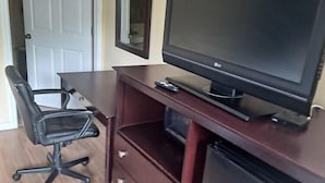 A room with a desk, a chair, a television, a mirror, and a small refrigerator.