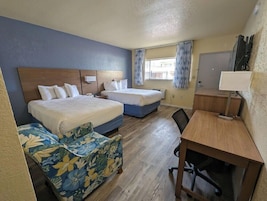 Quarto de hotel com duas camas, uma escrivaninha, uma cadeira e um sofá pequeno.
