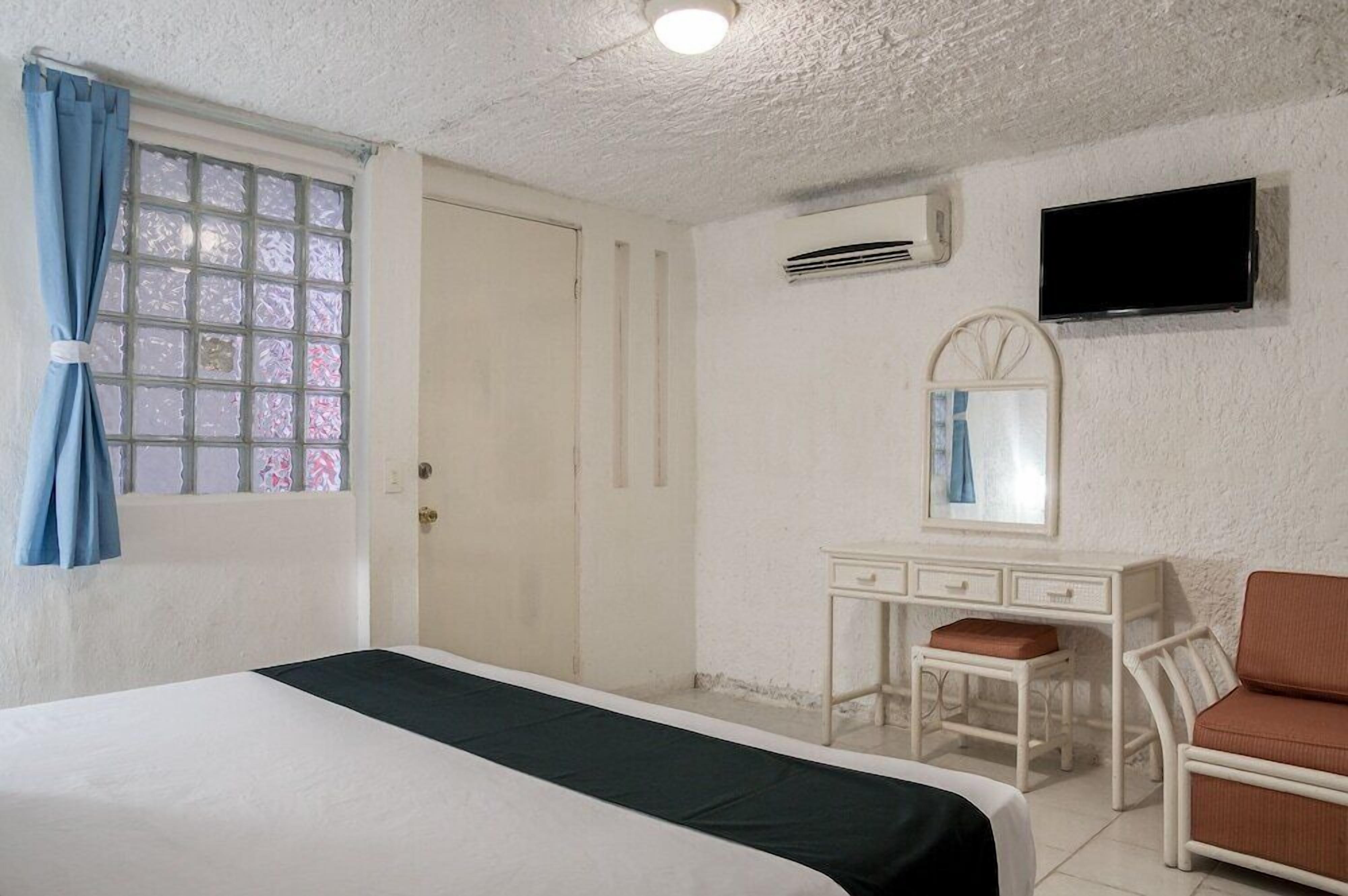Una habitación con una cama, un escritorio con una silla, un televisor y un equipo de aire acondicionado.