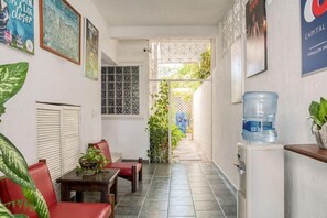 Un corridoio stretto con un distributore d'acqua, un tavolo con sedie e vista su un giardino attraverso un cancello.