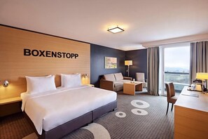 A hotel room with a large bed, a desk, a chair, a sofa, and a view of the city.