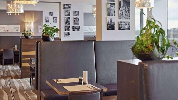 A modern hotel lobby with a seating area, wall-mounted photo displays, and a chandelier. - Lindner Hotel Nurburgring Congress (Nuerburg)