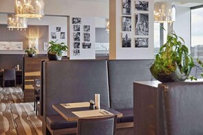 A modern hotel lobby with a seating area, wall-mounted photo displays, and a chandelier.