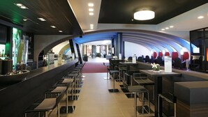 A modern restaurant with a curved ceiling, multiple seating areas, and a bar counter. - Lindner Hotel Nurburgring Congress (Nuerburg)