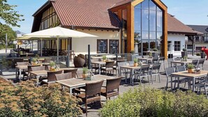 A restaurant with outdoor seating, a large glass window, and a traditional building facade. - Lindner Hotel Nurburgring Congress (Nuerburg)