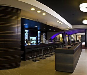A modern bar area with a long counter, bar stools, and a large island. - Lindner Hotel Nurburgring Congress (Nuerburg)