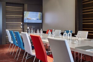 Un salón de conferencias con una larga mesa, varias sillas y un televisor instalado en la pared.