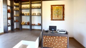A reception desk with a computer, a wall-mounted painting, and a shelf with pottery.