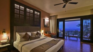 A hotel room with a large bed, a ceiling fan, a nightstand, a bedside table, and a view of the outdoors.