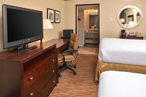 Habitación de hotel con televisión, escritorio, silla, cama y baño con espejo.