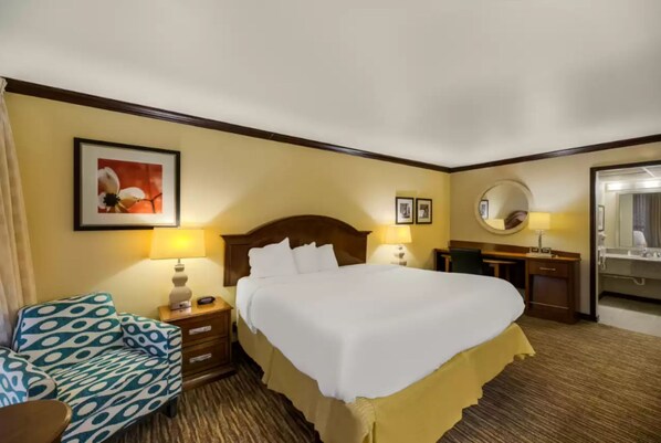 Habitación de hotel con una cama grande, un escritorio con silla, un espejo redondo y un cuadro en la pared.