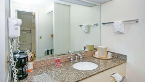 Un baño de hotel con encimera de granito, un lavabo, un espejo, un perchero para toallas y un secador de pelo.