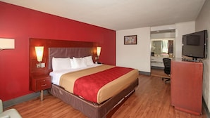 Una habitación de hotel con una cama grande, suelo de madera, un escritorio con una computadora y un televisor sobre un mueble.