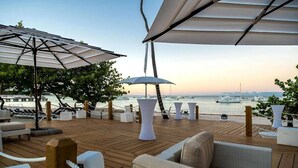 A wooden deck with outdoor seating, umbrellas, and a view of the sea and boats. - Blue Beach Punta Cana Luxury Resorts (Punta Cana)