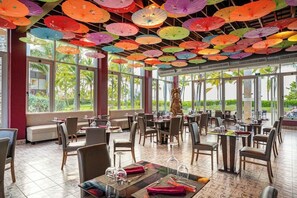 A restaurant with multiple tables and chairs, large windows, and colorful umbrellas hanging from the ceiling. - Blue Beach Punta Cana Luxury Resorts (Punta Cana)