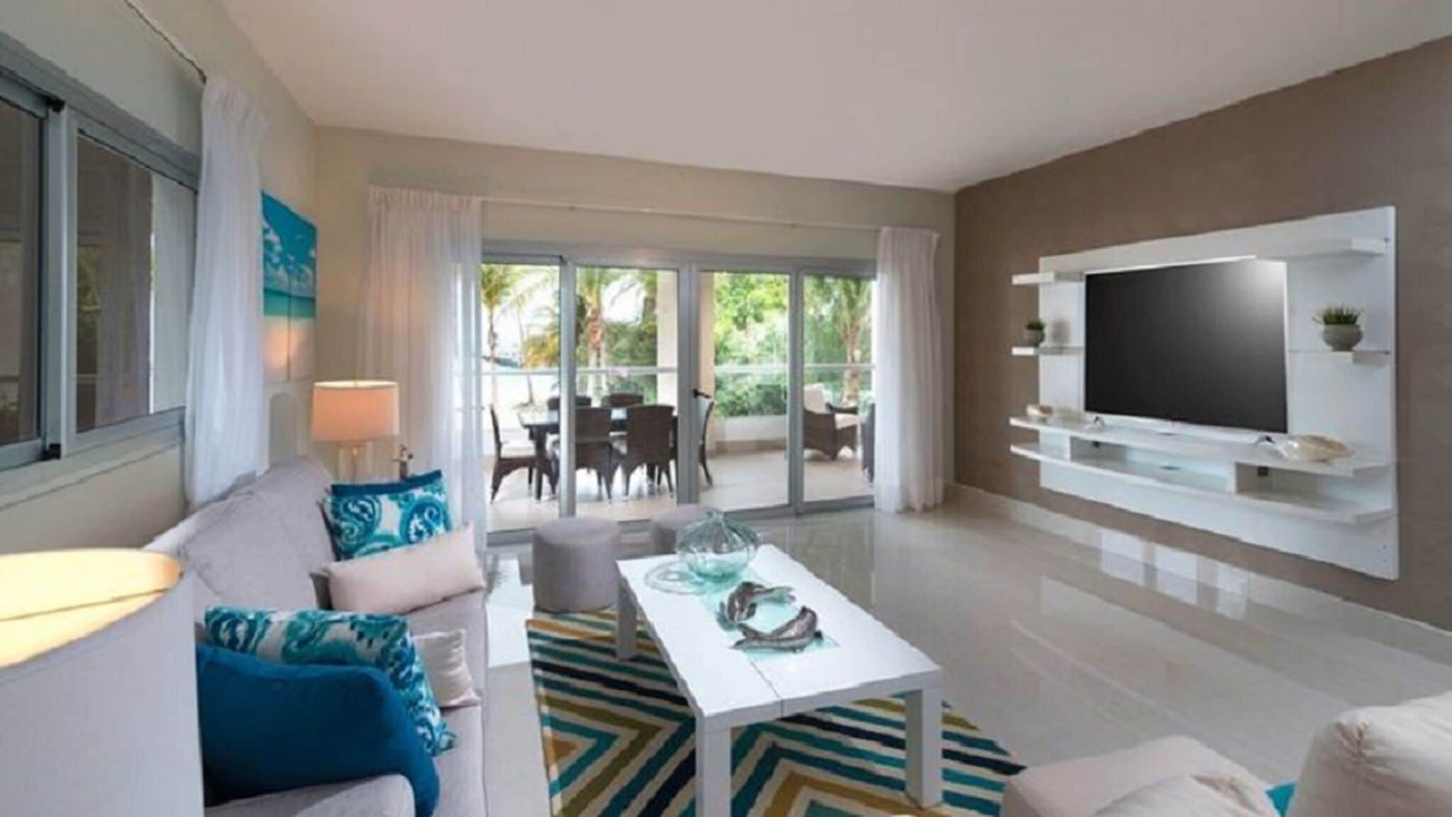 Un salon moderne avec un canapé, une table basse et un téléviseur. Il y a un balcon aménagé avec du mobilier d’extérieur.