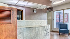 A reception desk with a clock, a wooden slatted door, and a blue chair.
