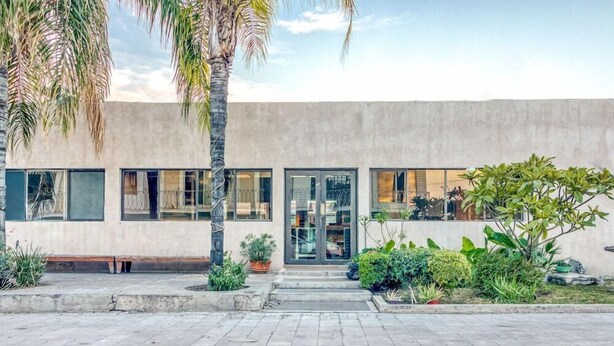 A modern building with a flat facade, large windows, and a paved entrance area with potted plants.