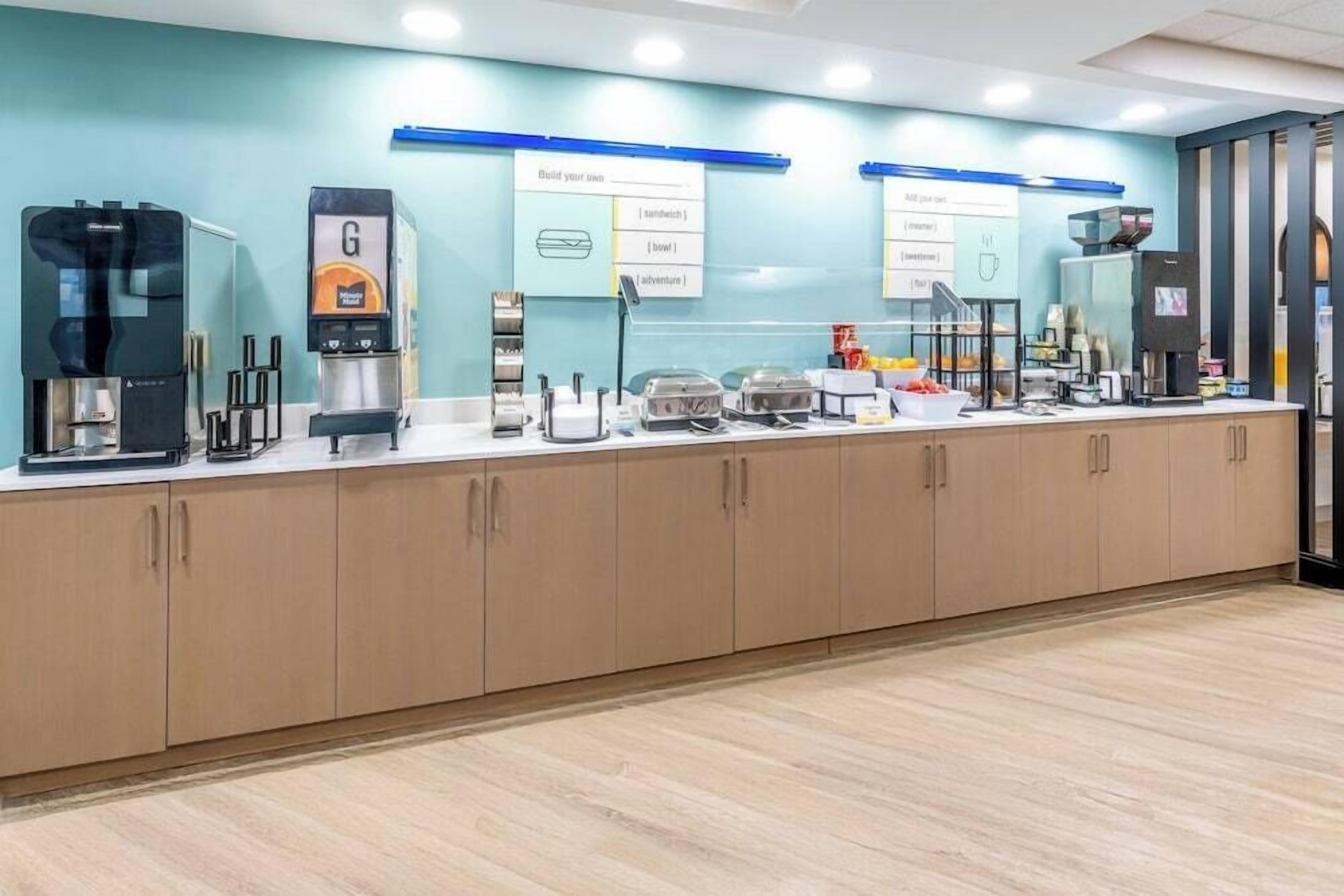 A long counter with coffee machines and food options, a whiteboard with menu items, and a view of the room.