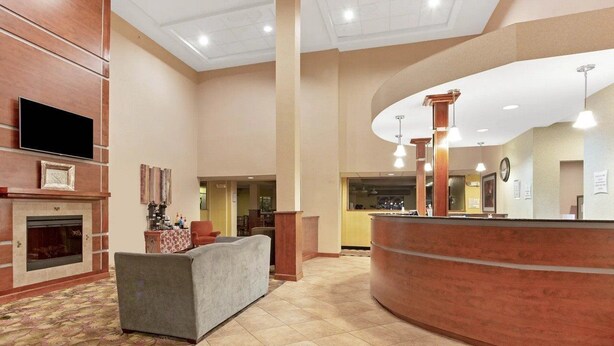 A lobby with a reception desk, a fireplace, a sofa, and a television. - La Quinta Inn Suites Richmond Kings Dominion (Doswell)