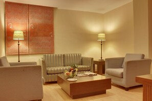 A living room with a sofa, armchairs, a coffee table with fruit, and two floor lamps. - Justa The Residence Hyderabad (Hyderabad)