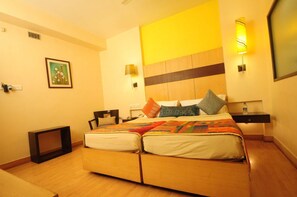 A hotel room with a bed, bedside tables, a nightstand, a wall-mounted lamp, a framed picture, and a small table. - Justa The Residence Hyderabad (Hyderabad)