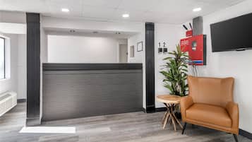 A reception area with a modern design, featuring a reception desk, a seating area with a chair, a plant, and a fire alarm cabinet.