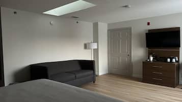 A hotel room with a bed, a sofa, a desk with a flat-screen TV, a lamp, and a wardrobe.
