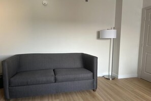 Ett rum med en grå soffa, en golvlampa och en dörr.