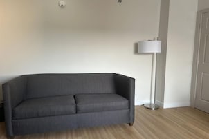Una habitación con un sofá gris, una lámpara de pie y una puerta.