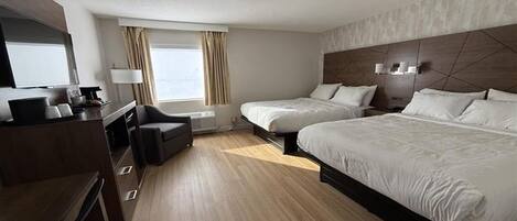 A hotel room with two beds, a desk, a chair, a TV, and a window with curtains.