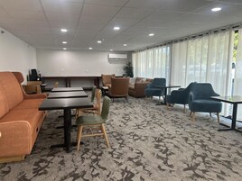 Habitación de hotel con sofá, sillas, mesa y un amplio ventanal con cortinas.