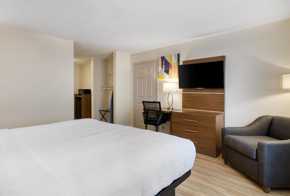 A hotel room with a large bed, a desk with a chair, a television, and a sofa. - Baldwin Inn & Suites, Surestay Collection by Best Western (West Springfield)
