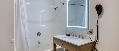 Une salle de bain équipée d’une douche, d’un lavabo, d’un miroir et d’un sèche-cheveux.