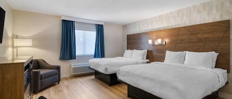 Ein Hotelzimmer mit zwei Betten, einem Schreibtisch, einem Stuhl, einem Fernseher und einem Fenster mit Vorhängen.