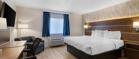 A hotel room with a bed, desk, chairs, and a TV.
