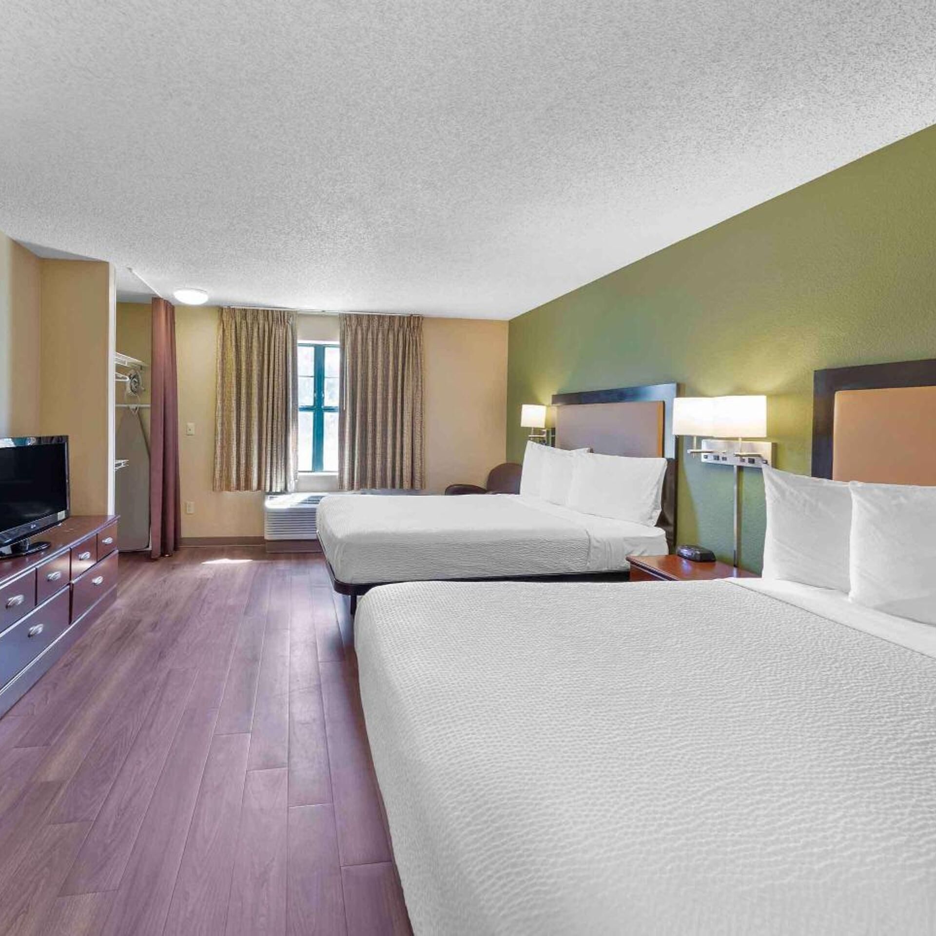 Une chambre d’hôtel avec deux lits, une télévision et une fenêtre avec des rideaux.