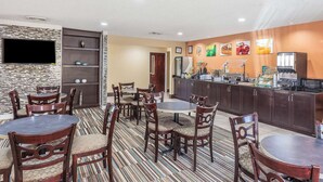 A hotel dining area with multiple tables and chairs, a kitchen counter with food items, and a flat-screen TV mounted on the wall. - Warsaw I-40 (Warsaw)