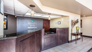 A reception area with a dark wood reception desk, a sign for Quality Inn by Choice Hotels, and a small table with a vase and decorative items. - Warsaw I-40 (Warsaw)