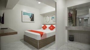 A modern hotel room with a bed, a desk, a mirror, and a painting on the wall.