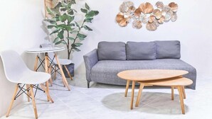 A modern living room with a grey sofa, two white chairs, a small round table, and a decorative wall piece.