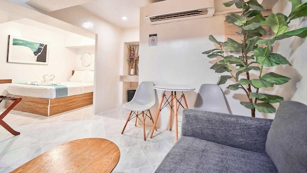 A modern hotel room with a bed, a small table, two chairs, a sofa, and a potted plant.