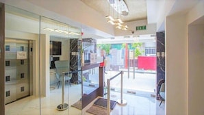 A modern hotel lobby with glass doors, a reception desk, and an exit sign.