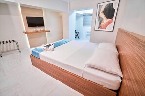 Ein modernes Hotelzimmer mit einem großen Bett, einem wandmontierten Fernseher, einer kleinen Sitzecke und Blick durch eine offene Tür.