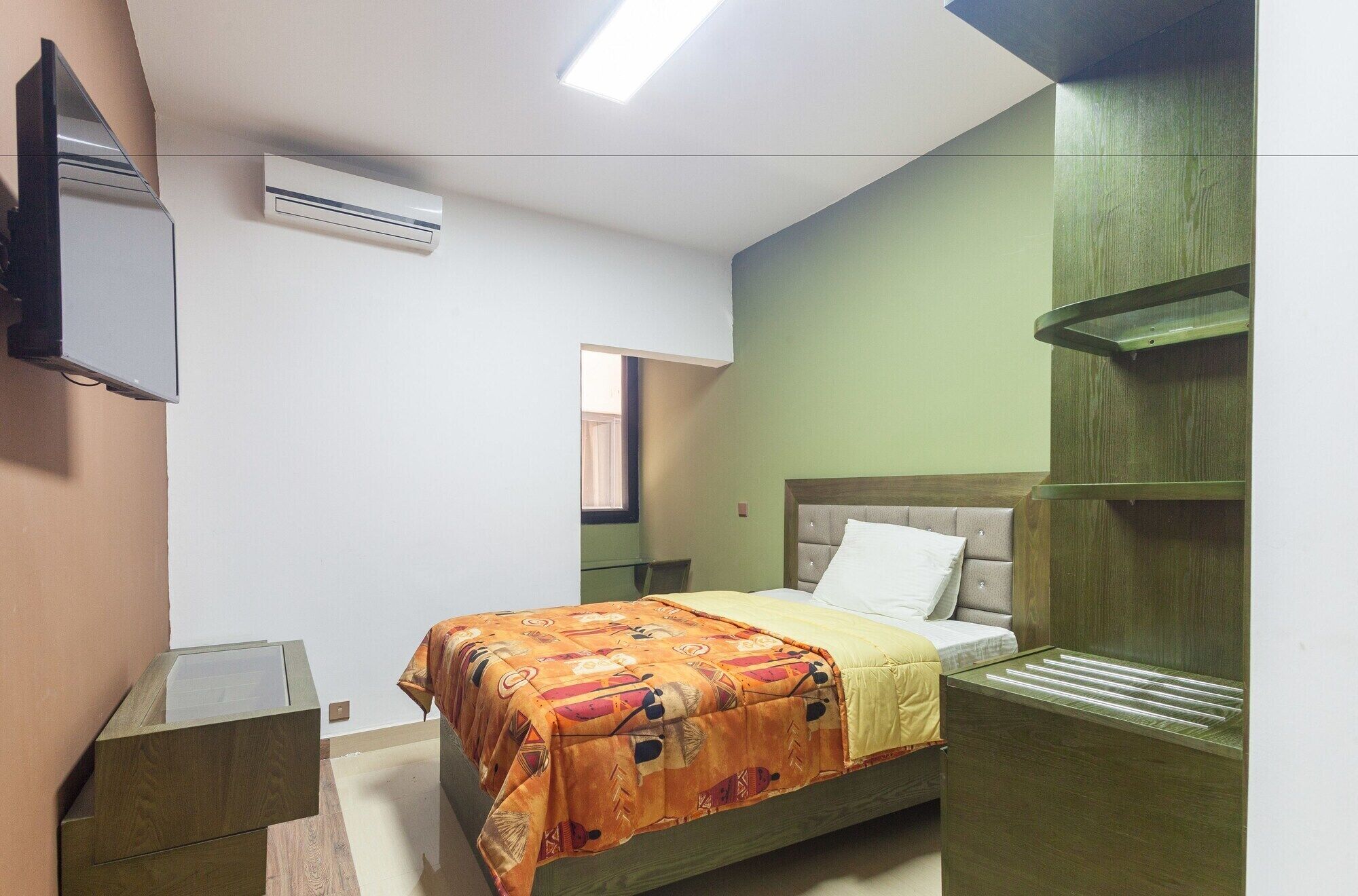 A bedroom with a bed, a bedside table, a mirror, and a wall-mounted air conditioner.