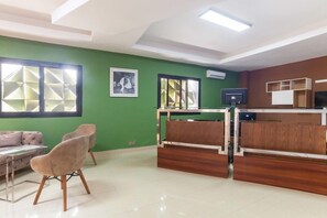 A reception area with a desk, chairs, a sofa, and a TV. - Wakola Hôtel Cheikh Anta (Dakar)