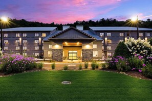 A hotel with a central entrance, multiple windows, and a well-maintained lawn with flowers. - Graystone Lodge, an Ascend Collection Hotel (Boone)
