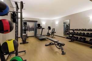 Un gimnasio con equipo de ejercicio, incluyendo una cinta de correr, banco de pesas y mancuernas.