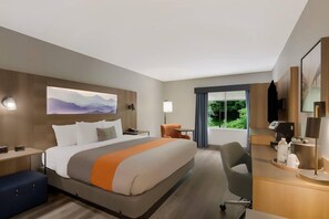 A hotel room with a large bed, a desk, a chair, a TV, and a window with a view of greenery. - Graystone Lodge, an Ascend Collection Hotel (Boone)